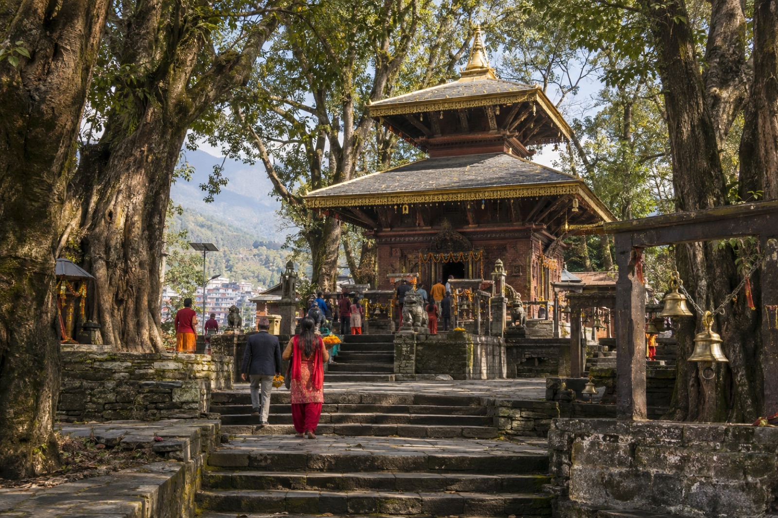 The pagoda-style Baglung Kalika Bhagwati Temple among old trees, with devotees on the stone steps