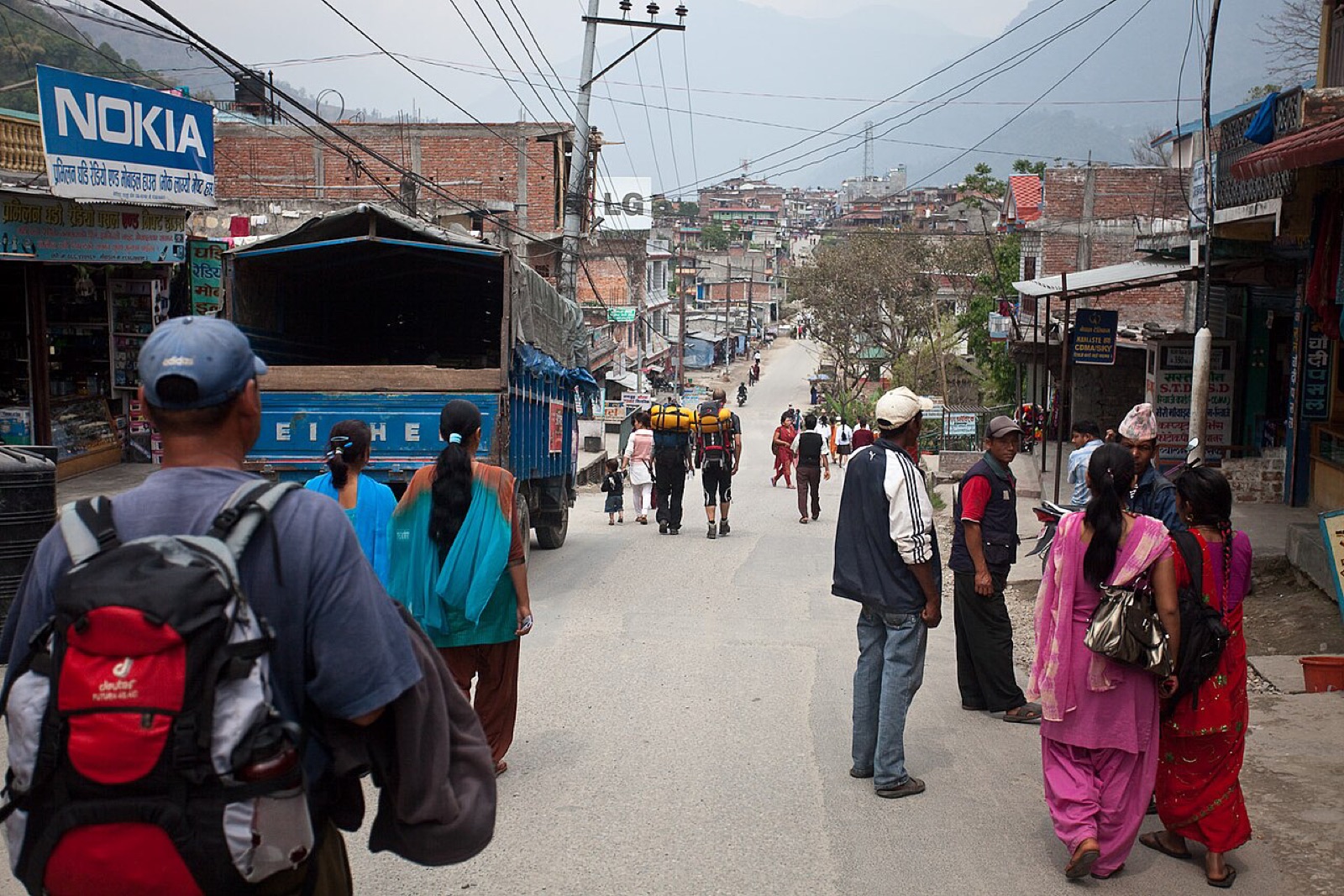 Trekkers with backpacks heading north up the main bazaar street of Besisahar, the Annapurna Circuit roadhead