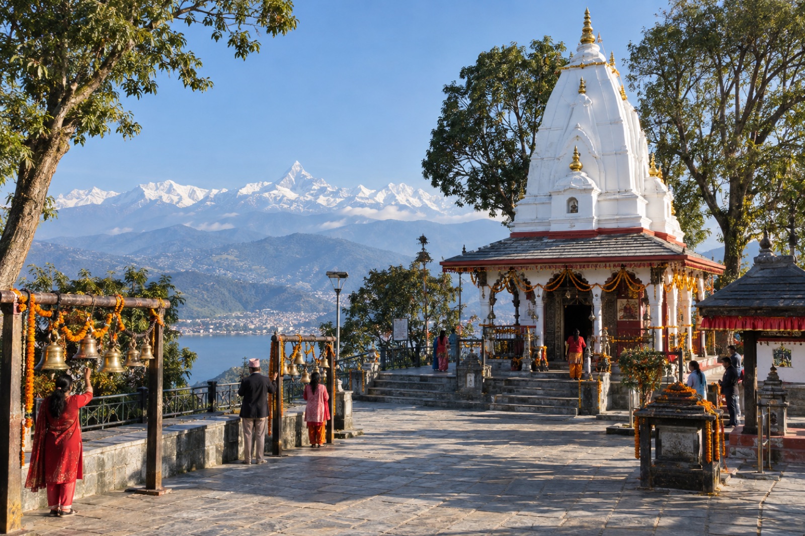 The white shikhara of Bindhyabasini Temple in Pokhara with bells, devotees and the Annapurna range behind