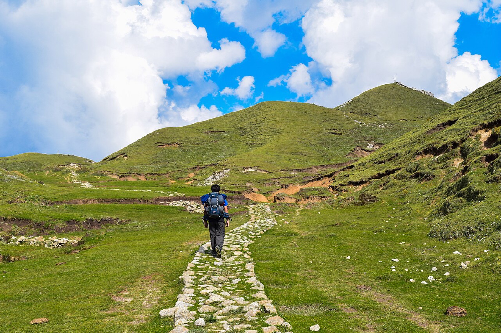 A trekker on the stone-paved trail across the grassy patan meadows of Khaptad National Park