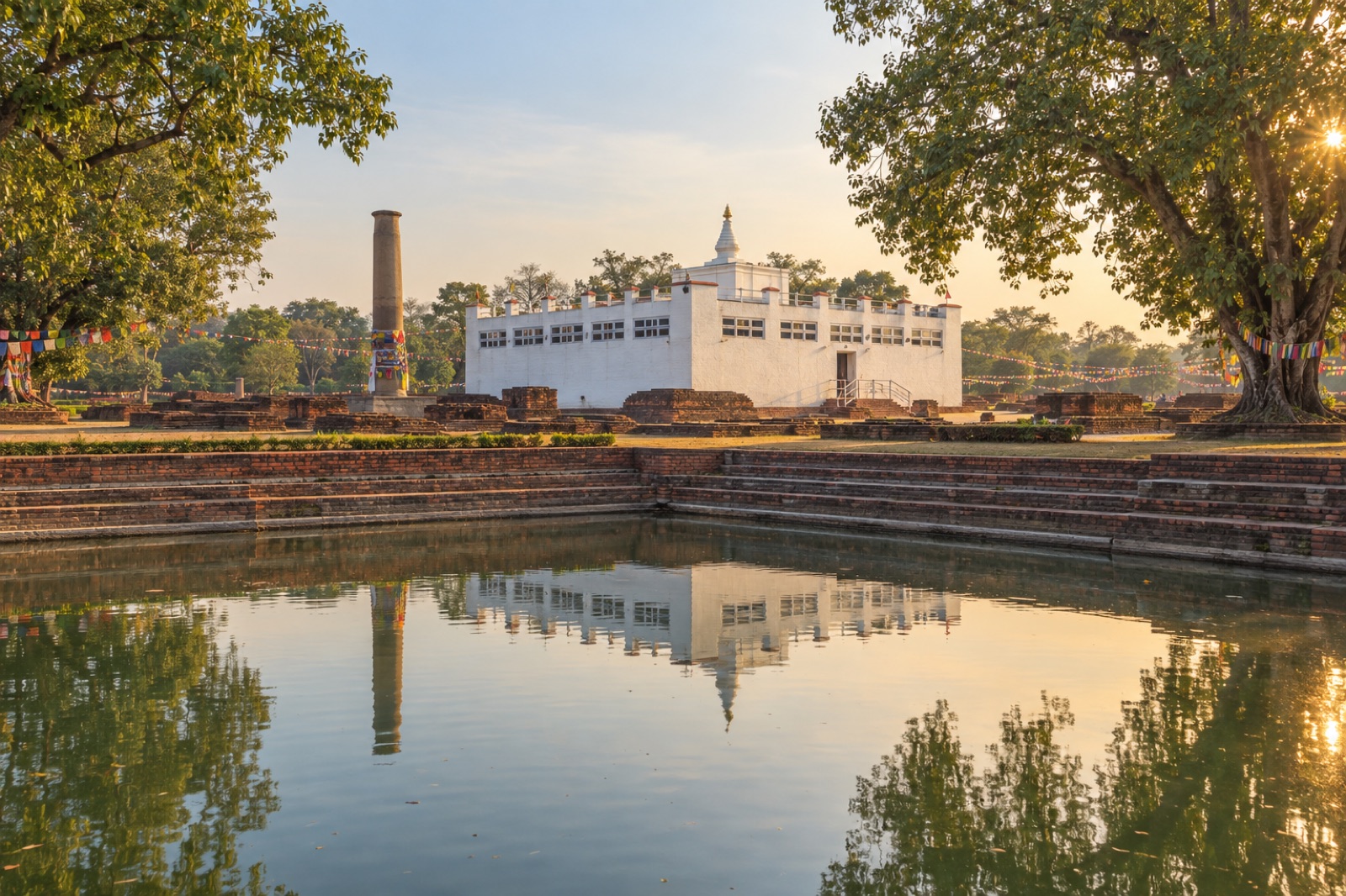 The white Maya Devi Temple and the Ashoka pillar reflected in the sacred pond at Lumbini