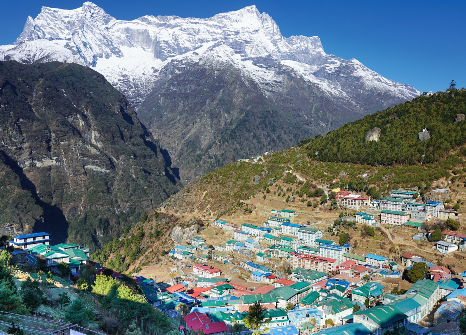 Namche Bazaar terraced up its horseshoe bowl under clear skies, with the snow face of Kongde Ri behind