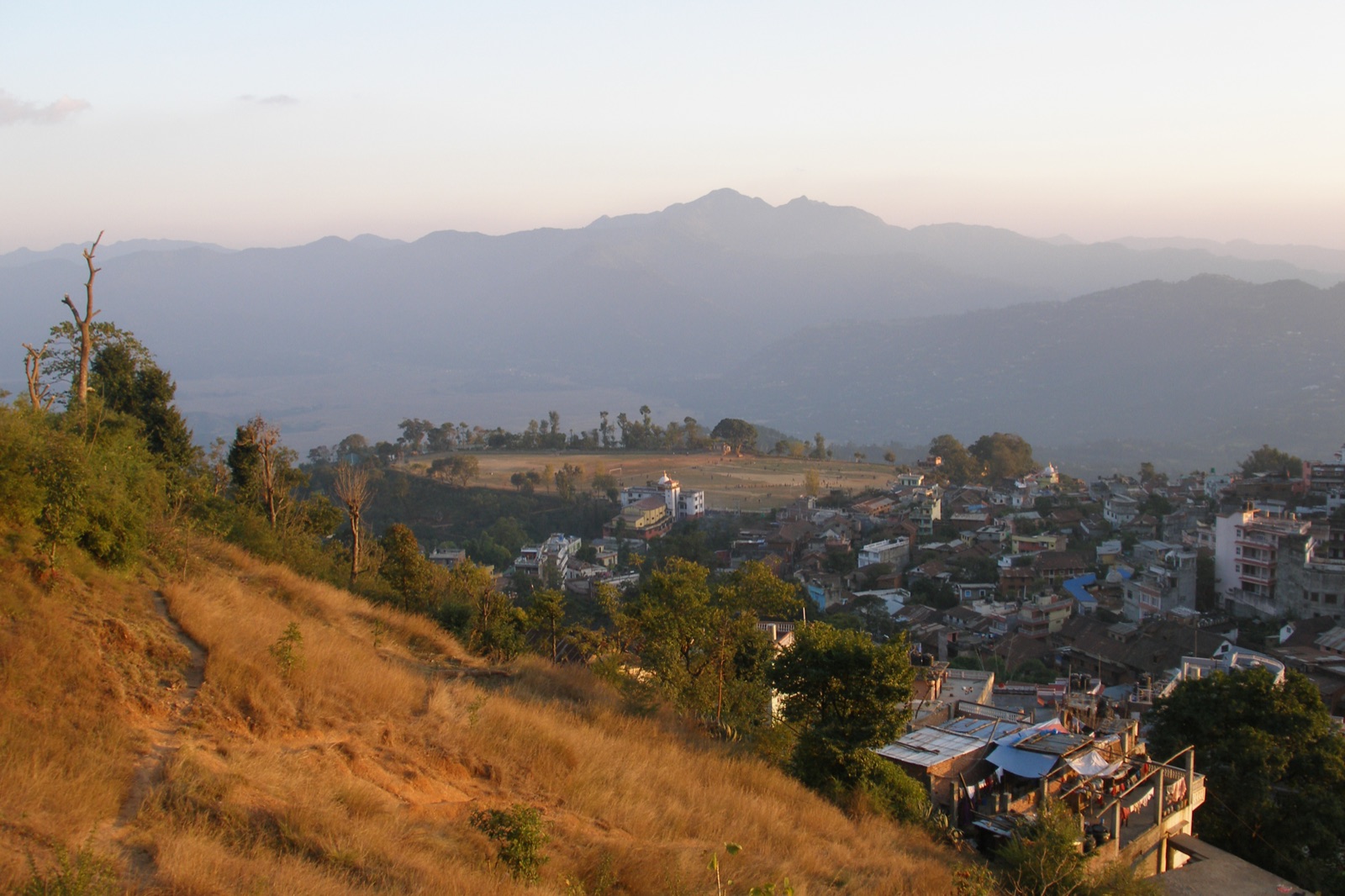 Tansen town spilling down its ridge in Palpa at sunset, rooftops above the Madi valley with hills behind